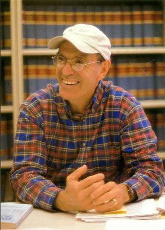 photo of Perry Zirkel, a smiling man wearing a plaid shirt, a tan baseball cap and glasses, seated at a table in front of shelves full of law books
